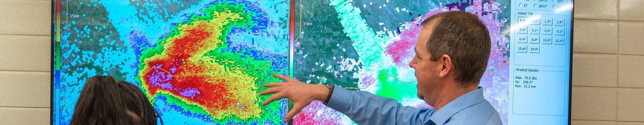 Instructor and student analyzing a weather radar display on a large screen.