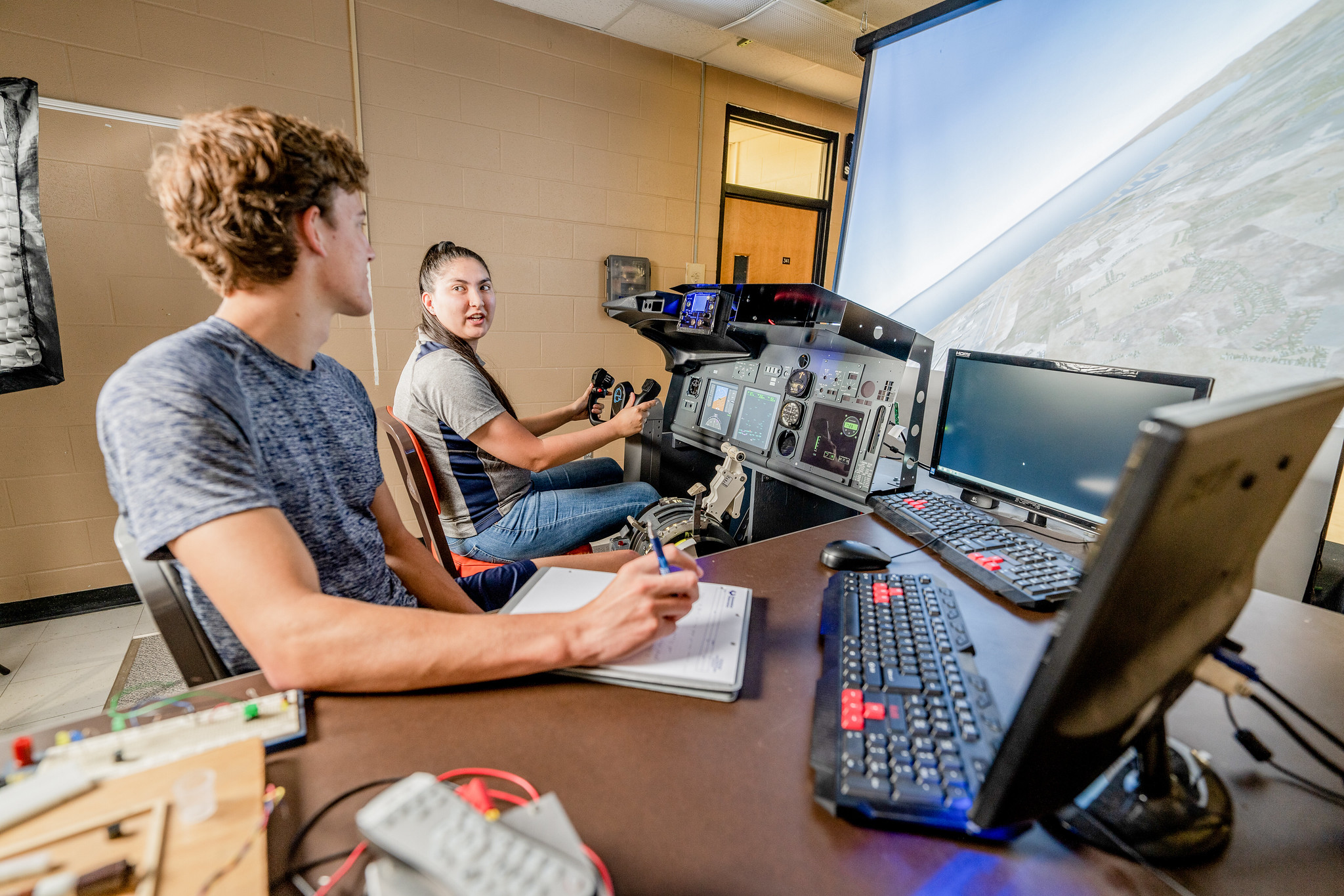Two students using a flight simulator and monitoring systems in a lab.