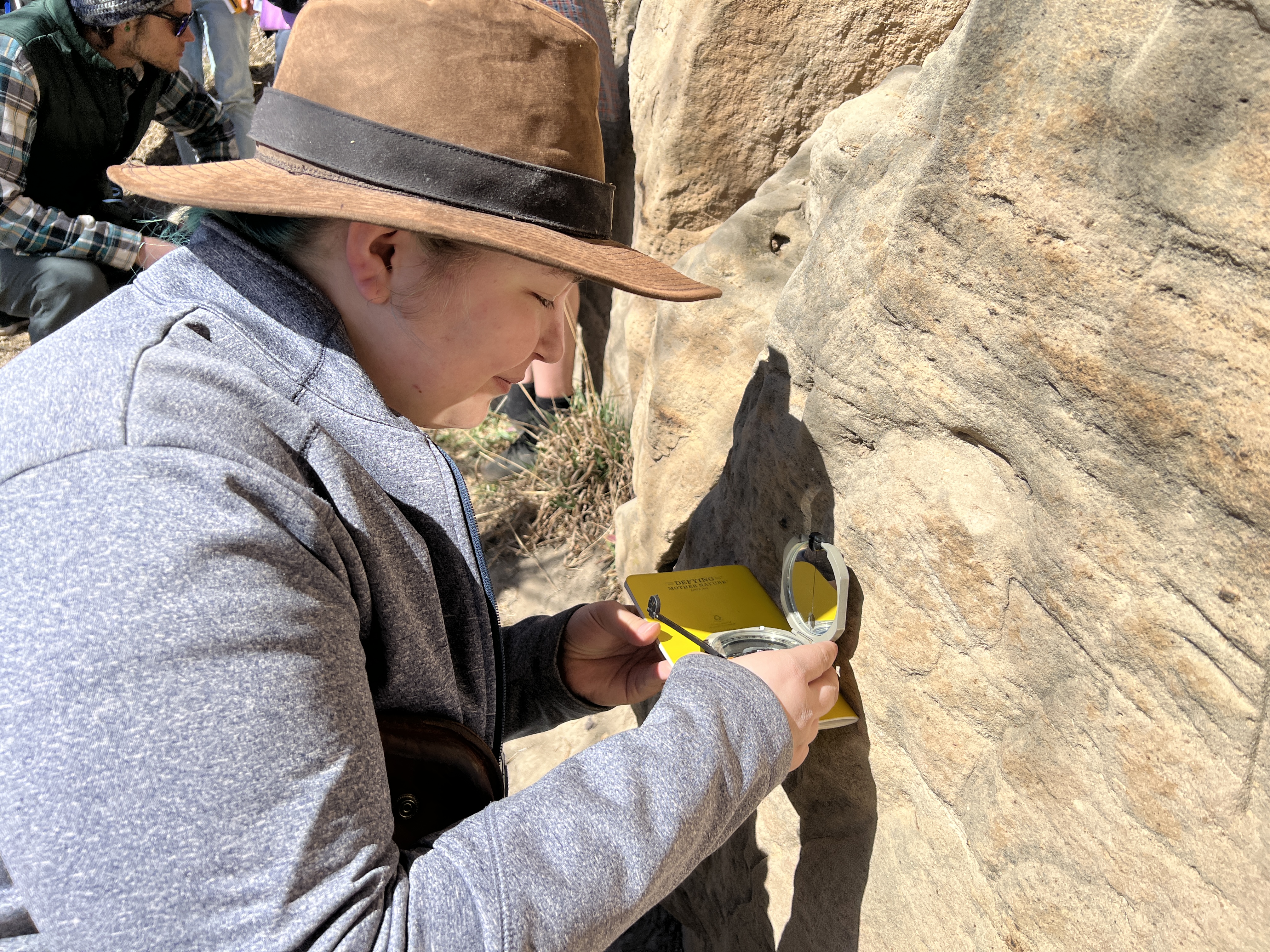 Geology fieldwork with a person inspecting rock formations using a tool.