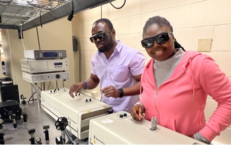 Two students working with laboratory equipment while wearing protective glasses.
