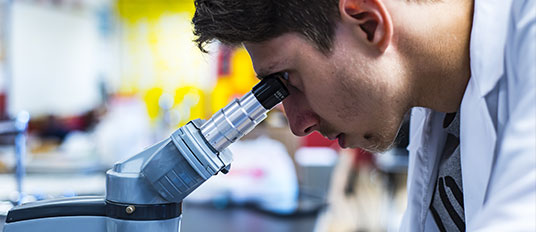 Biomedical Engineering Male Student Looking At Sample With Microscope